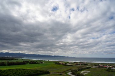 Görkemli bulutlar, yemyeşil alanlar üzerinde kıvrılarak kıyı şeridi boyunca sakin kıyı sularını karşılar..