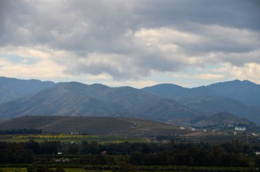 Yuvarlanan dağlar, aşağıdaki vadide canlı yeşilliğin üzerinde fırtınalı bir gökyüzüne karşı güzelce siluetlenmiştir..