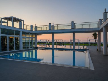 Sakin bir havuz kenarında gün batımının ılık renkleriyle parlayan alan, dinlenmek için huzurlu bir atmosfer yaratır..