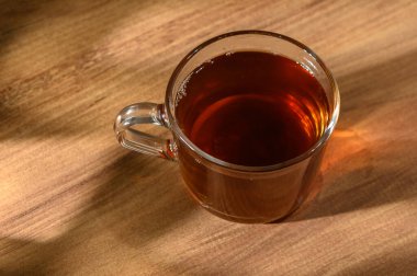 Dumanı tüten bir fincan çay, parlak ahşap bir yüzeye davetkar bir şekilde oturur ve rahatlatıcı bir öğleden sonranın özünü yakalar..