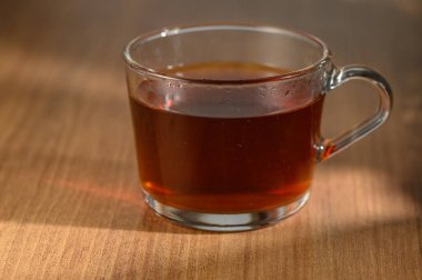 Konforlu bir ortamda, hafif güneş ışığıyla aydınlatılmış, bol bitkisel çayla dolu berrak bir fincan sergilenir..