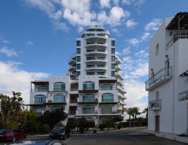 Çağdaş bir bina, berrak mavi bir gökyüzünün altında durmakta, dingin sahil kıyısında yemyeşil bir yere kurulmuş..