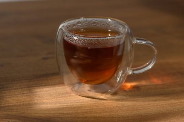 Bitki çayı berrak bir fincanda nazikçe buharlaşır, sıcak bir öğleden sonra güneşinde yıkanmış ahşap bir masada oturur..