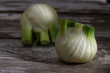 Dilimlenmiş yeşil soğanlar canlı yeşil üstlerini ve aşınmış ahşap bir masanın üzerinde duran katmanlı beyaz ampullerini sergiliyorlar..