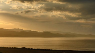 Altın güneş ışığı dingin gölü yıkıyor. Dağlar göründükçe sakin sulara yansıyor..
