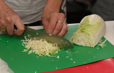Yetenekli bir aşçı taze lahana doğruyor yeşil bir kesme tahtasının üzerinde. Mutfak heyecanı ve öğrenmeyle çevrili..
