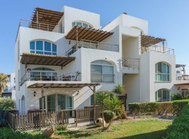 Açık mavi gökyüzünün altında sakin bahçelere bakan balkonları olan modern tasarımı olan çarpıcı bir sahil villası..