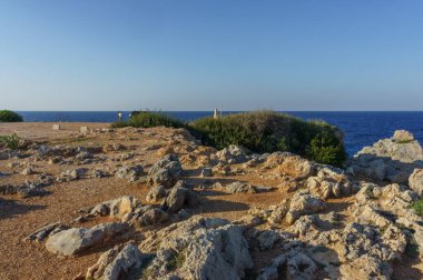 İki insan doğal güzelliği keşfederken kayalık bir manzara sakin okyanus dalgalarını canlı bir gökyüzüyle gözden geçirir..