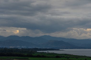 Yuvarlanan tepelerin üzerinde toplanan kara bulutlar, koydaki alacakaranlıkta sakin ama dramatik bir atmosferi yansıtıyor..