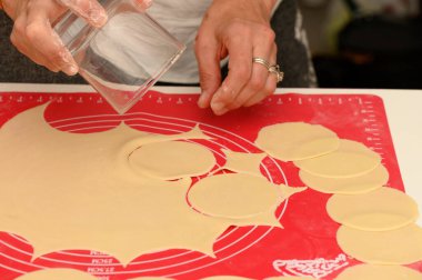 Taze makarna çemberleri, yetenekli ellerin aşçılık ve adanmışlık sergilediği parlak kırmızı bir paspasın üzerinde açılır..