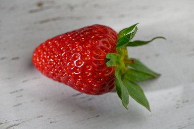 Canlı kırmızı bir çilek eskimiş ahşap bir masanın üzerinde duruyor. Parlak dokusunu ve taze yeşilliklerini sergiliyor..