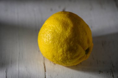 Canlı bir limon yıpranmış bir masada tek başına oturur. Yumuşak bir ışıkta güneşlenir..