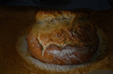 Zanaatkar ekmeği parşömen üzerinde sevgiyle serinliyor, altın kabuğunu ve kırsal cazibesini yumuşak ışıkta sergiliyor..