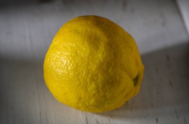 Canlı bir limon, eskimiş ahşap bir masaya davetkar bir şekilde oturmuş taze, lezzetli dokusunu ve rengini sergiliyor..