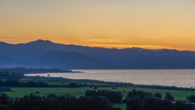 Yumuşak alacakaranlık yemyeşil tarlaları sarıyor. Dalgalar sakin kumsalda nazikçe süzülüyor, doğanın güzelliğini vurguluyor..
