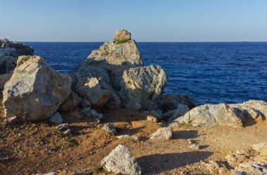 Güneş, pürüzsüz kayaların üzerinde sıcak bir parıltı yayıyor. Yumuşak dalgalar barışçıl Akdeniz kıyılarına doğru süzülüyor..