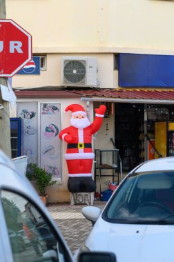 Dolu bir dükkanın önünde neşeli kırmızı, şişme Noel Baba dalgaları, gün batımında yoldan geçenlere bayram neşesi getiriyor..