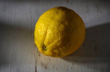 Canlı bir limon, dokulu bir yüzeyde oturur. Günün yumuşak ışığında tazelik ve sadelik yayar..