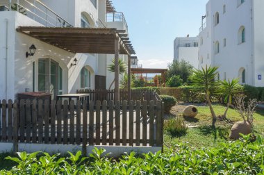 Sakin bir açık alan, canlı yeşillik ve modern mimarinin ortasında ahşap bir pergola barındırır. Rahatlamayı davet eder..