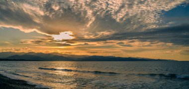 Altın renkler ufku aydınlatır. Yumuşak dalgalar kıyıya vurur. Huzurlu bir akşam atmosferi yaratır..