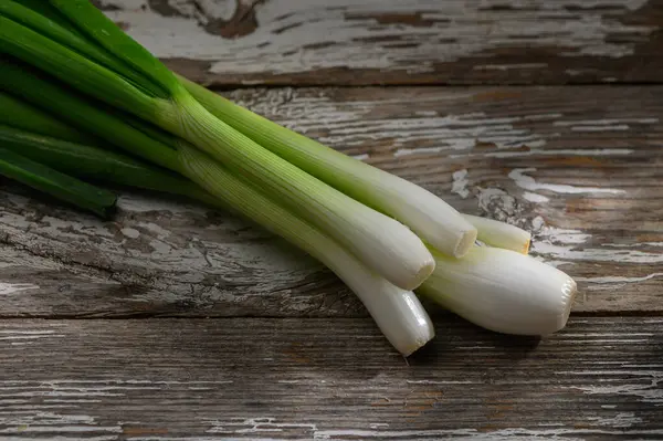 Canlı yeşil soğanlar yıpranmış ahşabın üzerinde dinleniyor, taze görünüşlerini ve yemek pişirmek için çekici dokularını sergiliyorlar..