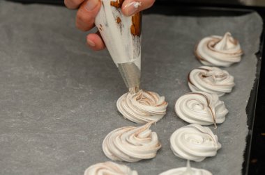 Tatlı krema kıvrımları, sıcak bir mutfakta pişirilmeye hazır bir tepsiye dikkatlice boruladıkları zaman şekillenir..