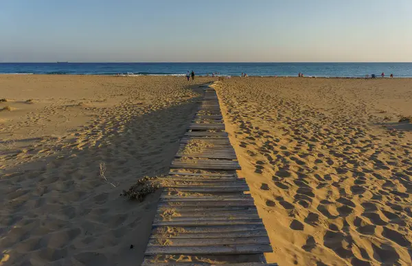 Kumlu sahil boyunca uzanan kırsal bir sahil yürüyüşü, ziyaretçileri sakin, parıldayan denize davet ediyor..