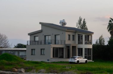 Şık konut yeşilliğin ortasında duruyor, alacakaranlık gökyüzüne yumuşak renkler saçarken suya bakıyor..
