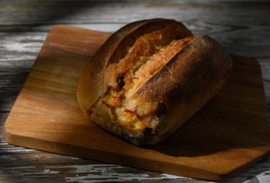 Altın kabuklu ekmek ahşap bir tahtanın üzerinde soğur, zanaatkar dokusunu ve ılık tonlarını hafif güneş ışığında vurgular..