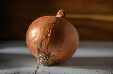 Köy soğanı yıpranmış ahşap bir masada oturur, sıcak, doğal ışıkla aydınlatılır, eşsiz dokusunu sergiler..
