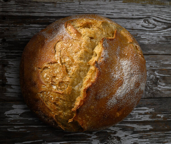 A beautifully crafted round loaf sits on a textured wooden tabletop, exuding warmth and inviting flavors.