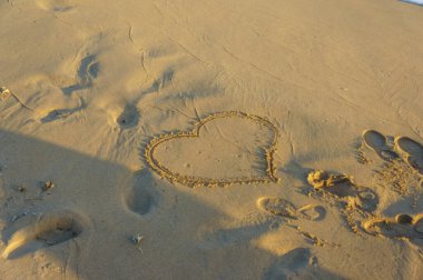 Sıcak kuma kazınmış bir kalp şekli, alacakaranlıkta sakin bir sahilde yumuşak ayak izleriyle çevrili..