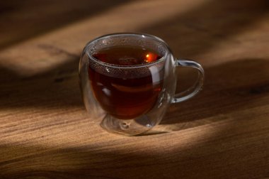 Bir fincan buharlı çay, kırsal bir ahşap masada dinleniyor. Öğleden sonra güneşinde rahatlamaya ve sıcaklığa davetiye çıkarıyor..