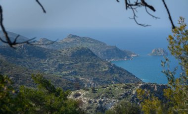 Yumuşak yamaçlar, yemyeşil ve kayalık çıkıntıların çerçevelediği berrak bir gökyüzünün altında sakin denizle buluşur..