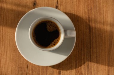 Dumanı tüten bir kahve fincanı, ahşap bir yüzeyde narin bir şekilde duruyor, sabah ışığının yumuşak parıltısında güneşleniyor..