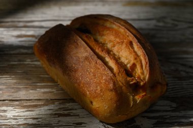 Altın hamurlu taze fırınlanmış somun, yaşlanmış ahşabın üzerinde yatıyor, öğleden sonra güneşinin yumuşak parıltısında güneşleniyor..