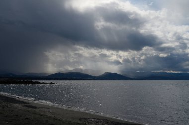 Dalgalanan suların ışığı yansıttığı sakin bir göl üzerinde dramatik bir gökyüzü beliriyor, çarpıcı bir akşam atmosferi yaratıyor..