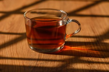 Çaydan buhar yükselir, kırsal ahşap masada büyüleyici gölgeler bırakır öğleden sonra ışığı filtrelerken.