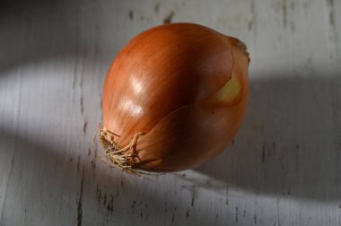 Tek bir soğan, doğal parlaklığını vurgulayan yumuşak ışıkla aydınlatılmış, eski ahşap bir yüzeyde yatar..