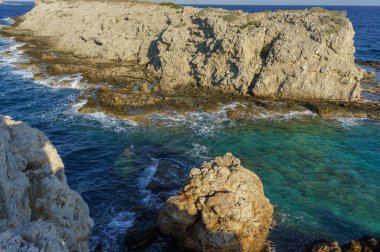 Engebeli uçurumlar, batan güneşin sıcacık parıltısıyla boyanmış berrak turkuaz sulardan keskin bir şekilde yükselir..