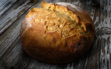 Altın kabuklu sanatsal ekmek, yıpranmış ahşap bir masaya davetkar bir şekilde oturur, sıcaklık ve lezzet saçar..