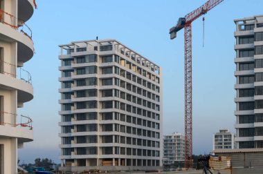 Aktif bir inşaat bölgesinde modern mimari sergilenen alacakaranlık gökyüzüne karşı yeni yerleşim binaları ortaya çıkıyor..