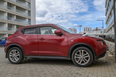 Gaziveren Kıbrıs Rum Kesimi -28.02.2025 Çarpıcı kırmızı bir SUV bulutlarla dolu canlı bir gökyüzü altında çağdaş mimari yakınlarında park halinde duruyor.