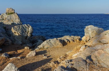 Sakin bir bakış açısı, alacakaranlık saatlerinde derin mavi denize bakan engebeli kayaları ortaya çıkarır..