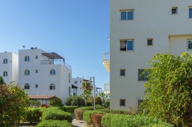 Saf beyaz binaların üzerinde, sakin bir yerleşim bölgesinde canlı yeşillikler tarafından kucaklanan güneş ışığı çağlayanı..