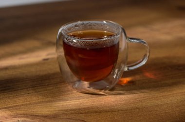 Sıcaklık, ahşap dokunun davetkar arkaplanına karşı koyan, zengin çayla dolu bir bardaktan yayılır..