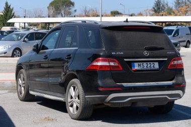 Gaziveren Kıbrıs Rum Kesimi - 15.03.2025 Açık bir günde, yemyeşil ve diğer park halindeki arabalarla çevrili parlak bir park yerinde parlak siyah bir SUV dinleniyor.