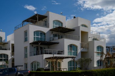 Güneşli beyaz binalar, bereketli yeşilliklerle çevrili mavi bir gökyüzünün altında zarif bir şekilde duruyor..