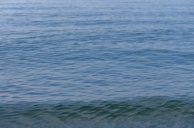 Yumuşak güneş ışığı sakin sularda dans eder. Gün ortasında kıyı şeridi boyunca huzurlu bir atmosfer yaratır..