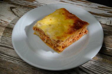 Ağız sulandıran bir dilim peynirli makarna beyaz bir tabakta duruyor, zengin malzemelerini ve dokularını sergiliyor..